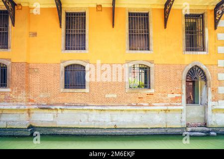 facade with windows covered with bars in Venice with a canal with green water Stock Photo