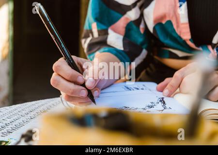 detail unrecognizable caucasian woman on terrace of her house by day, drawing with black sketch marker in a notebook on the table, close-up, copy spac Stock Photo