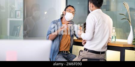 Two office workers talking while coffee break in new normal office panorama. Stock Photo