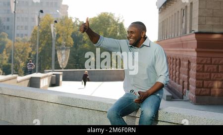 Elderly ethnic middle-aged man in city greeting friend waving hand. African middle-aged male on meeting date invite come here welcome gesture Stock Photo