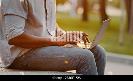 Closeup male hands texting working on wireless laptop device in city. Unrecognizable African ethnic businessman sit outdoors typing to client on Stock Photo