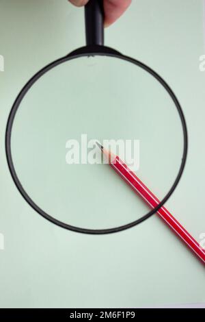 One red pencil under a magnifying glass close-up on a light background. Stock Photo