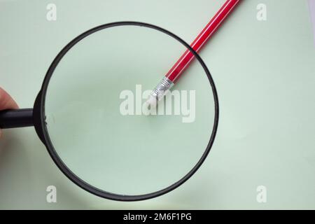 One red pencil under a magnifying glass close-up on a light background. Stock Photo