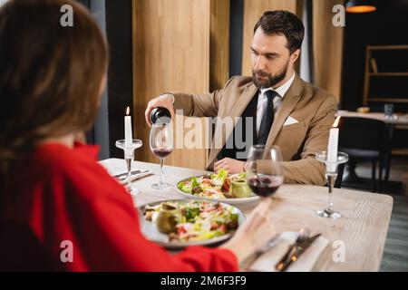 bearded man pouring red wine in glass near girlfriend during dinner on valentines day,stock image Stock Photo