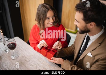 overhead view bearded man in formal wear holding present while cheerful woman in red dress pulling ribbon,stock image Stock Photo