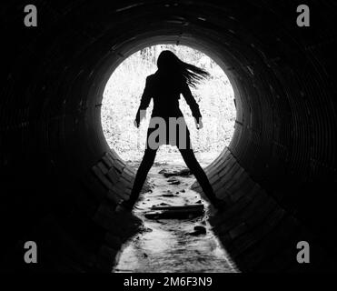 Silhouette of a young woman in the coc of the tunnel. A sewer tunnel under the road. Stock Photo