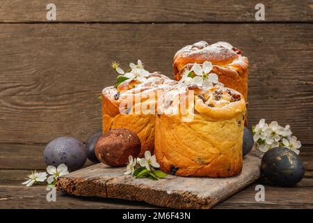 Easter cake Cruffin or sweet bread kulich with painted eggs. Traditional festive baking and fresh cherry flowers, festive wooden background. Vintage b Stock Photo