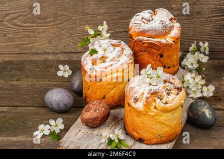 Easter cake Cruffin or sweet bread kulich with painted eggs. Traditional festive baking and fresh cherry flowers, festive wooden background. Vintage b Stock Photo