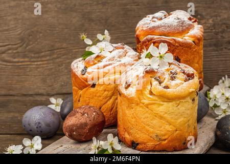 Easter cake Cruffin or sweet bread kulich with painted eggs. Traditional festive baking and fresh cherry flowers, festive wooden background. Vintage b Stock Photo