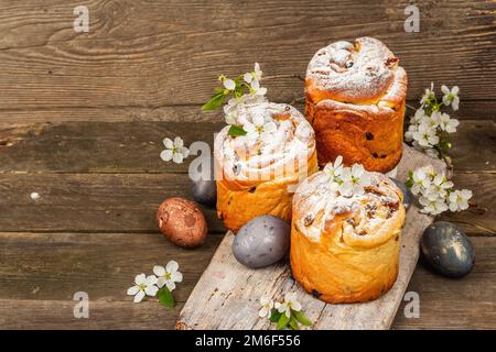 Easter cake Cruffin or sweet bread kulich with painted eggs. Traditional festive baking and fresh cherry flowers, festive wooden background. Vintage b Stock Photo