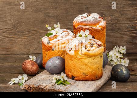 Easter cake Cruffin or sweet bread kulich with painted eggs. Traditional festive baking and fresh cherry flowers, festive wooden background. Vintage b Stock Photo