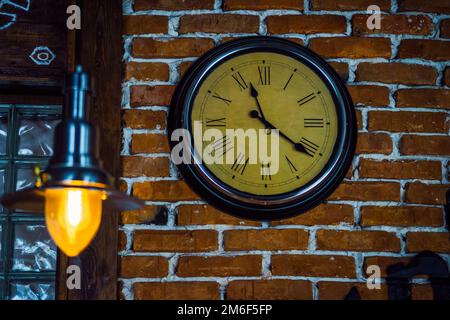 Round clock with Roman numerals hang on brick wall Stock Photo