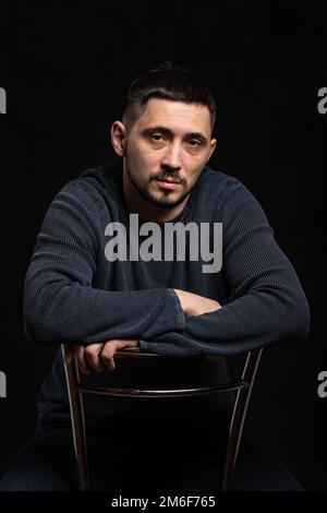 Portrait of a man of thirty years of Caucasian appearance in a regular sweater on a black background Stock Photo