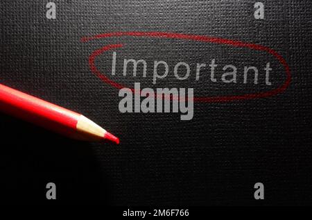 Important text circled in red pencil on black textured paper background Stock Photo