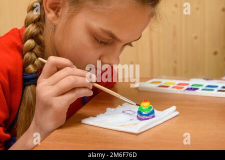 A girl carefully paints a figurine made of salt dough Stock Photo
