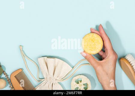 Female hand with solid shampoo bar. Bath accessories lying on a light blue background. Plastic free, zero waste living, low water ingredients. Stock Photo