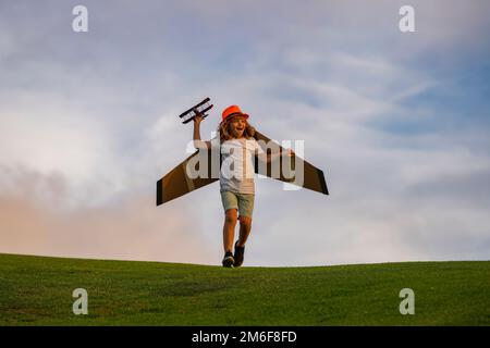 Happy childhood. Kid having fun with toy airplane in field. Child pilot aviator with airplane dreams of traveling in summer in nature. Stock Photo