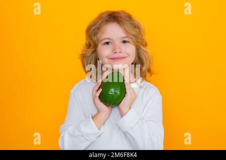 Vitamin and healthy fruits for kids. Kid hold red avocado in studio. Studio portrait of cute child with avocado isolated on yellow background. Stock Photo