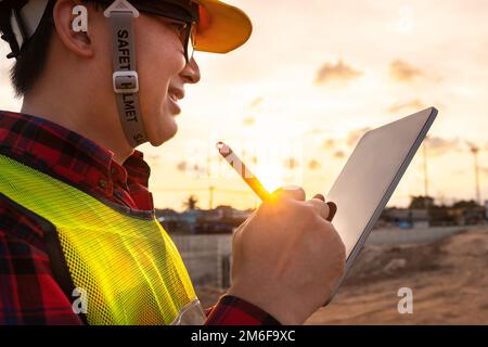 asian technician civil engineer use tablet with smart pen technology on transport site construction to inspect blueprint engineering work online with Stock Photo