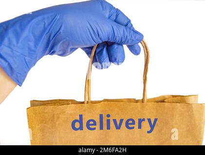 A hand in a blue rubber glove holds a paper bag labeled DELIVERY, fast food delivery concept, isolated on a white background by Stock Photo