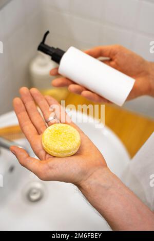 Man is choosing between a solid shampoo bar and a liquid one. Bathroom accessories. Sustainable hair care. Plastic free, zero waste living, low waste Stock Photo