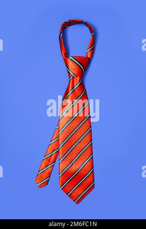 Red men's striped tie taken off for leisure time, isolated on blue background. Stock Photo