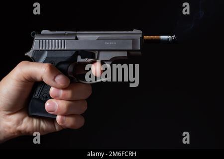 Concept of harm to smoking, smoking kills, A gun shooting a cigarette on a black background. Stock Photo