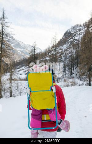 Man and woman with a baby in a backpack carrier walking in the field in a mountain snowy landscape Stock Photo