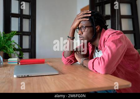 Upset young African guy freelancer touching forehead thinking about personal problems at workplace Stock Photo