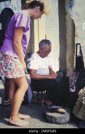 Historic Archive Image Of A Young Female Having Her Shoes Repaired By An Elderly Chinese Shoe Repairer, Cobbler On The Streets Of Chinatown,Singapore 1990 Stock Photo