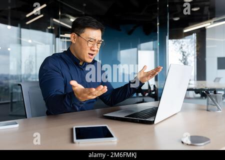 Angry and upset asian businessman, man working with laptop unhappy with result achievement, man inside office disappointed. Stock Photo
