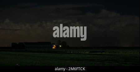 Haunting night scene of a farmhouse in the countryside with towering storm clouds in the background. Stock Photo