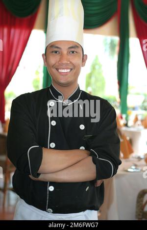 asian chef confidence posing and smiling at work in restaurant wearing uniform and hat or cap looking at camera Stock Photo