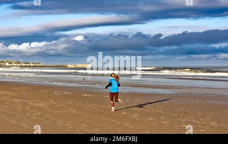 Lossiemouth East Beach Moray coast Scotland a blue sky white clouds and surf and a runner on the sands in winter Stock Photo