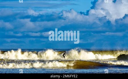 Lossiemouth East Beach Moray coast Scotland lone surfer and breaking waves in winter Stock Photo