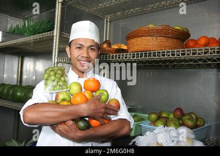 young chef holding fruits smiling look at camera in fridge Stock Photo