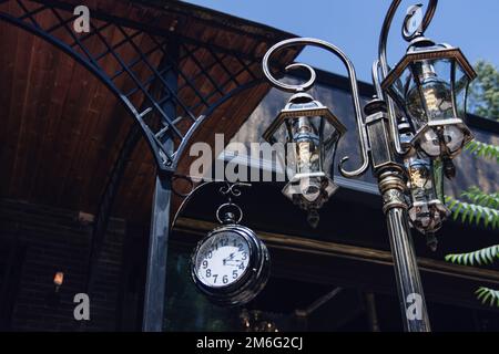 Wrought-iron decorative lamppost and a large clock at the entrance to the restaurant Stock Photo
