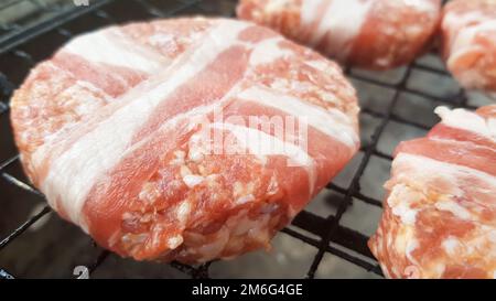 Raw meat cutlets wrapped in bacon are cooked on the grill rack. The chef prepares the grilled burger patties. Ingredients for ma Stock Photo
