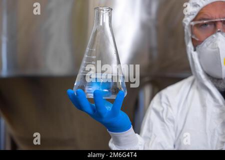 Serious brewery technologist demonstrating a glass vessel before the camera Stock Photo