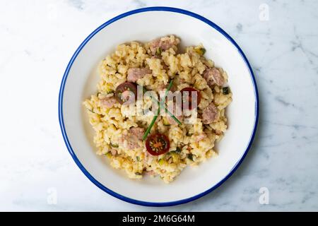 Risotto with pork sausage and cherry tomatoes. Risotto is a northern Italian rice dish cooked with broth until it reaches a creamy consistency. Stock Photo