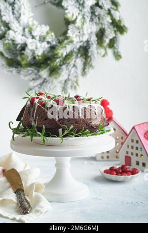 Christmas chocolate bundt cake. Traditional Christmas fruit cake with white glaze, cranberries and rosemary on white stand with Christmas decoration. Stock Photo