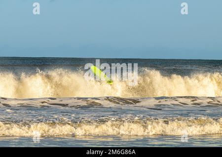 Green surfboard without surfer on the sea at Cayton Bay, North Yorkshire, UK Stock Photo