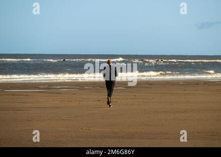 Rear view of a caucasian male runner on the beach at Cayton Bay in North Yorkshire, UK. Stock Photo