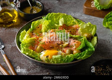 Salmon salad - smoked salmon hard boiled eggs, olives, watercress, sesam and green vegetables on dark brown table. Healthy food. Clean Eating. Paleo d Stock Photo