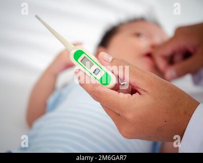 Baby illness medicine flu fever and thermometer, a doctor checks the temperature of the ill baby. Digital thermometer to measure the heat temperature Stock Photo