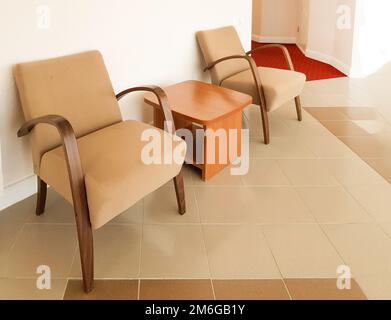 Two brown armchairs and a coffee table between them against a pink wall, a modern interior of a living room or hall in a hotel Stock Photo