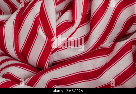See closeup of red and white stripe fabric in rolls, curves, folds. Dimensional background material with texture is seen in horizontal or vertical. Stock Photo