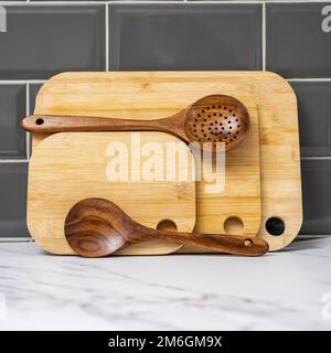 stack of bamboo chopping boards and teak hardwood spoons lined up against grey tiled walls Stock Photo