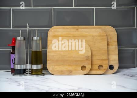 glass bottles with pouring spouts for olive oil balsamic vinegar with bamboo boards on granite worktop with chilli bottle Stock Photo