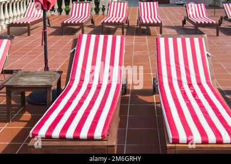 Empty wooden deck chairs with red and white striped mattresses stand in a row. Luxury outdoor recreation, sunshine Stock Photo